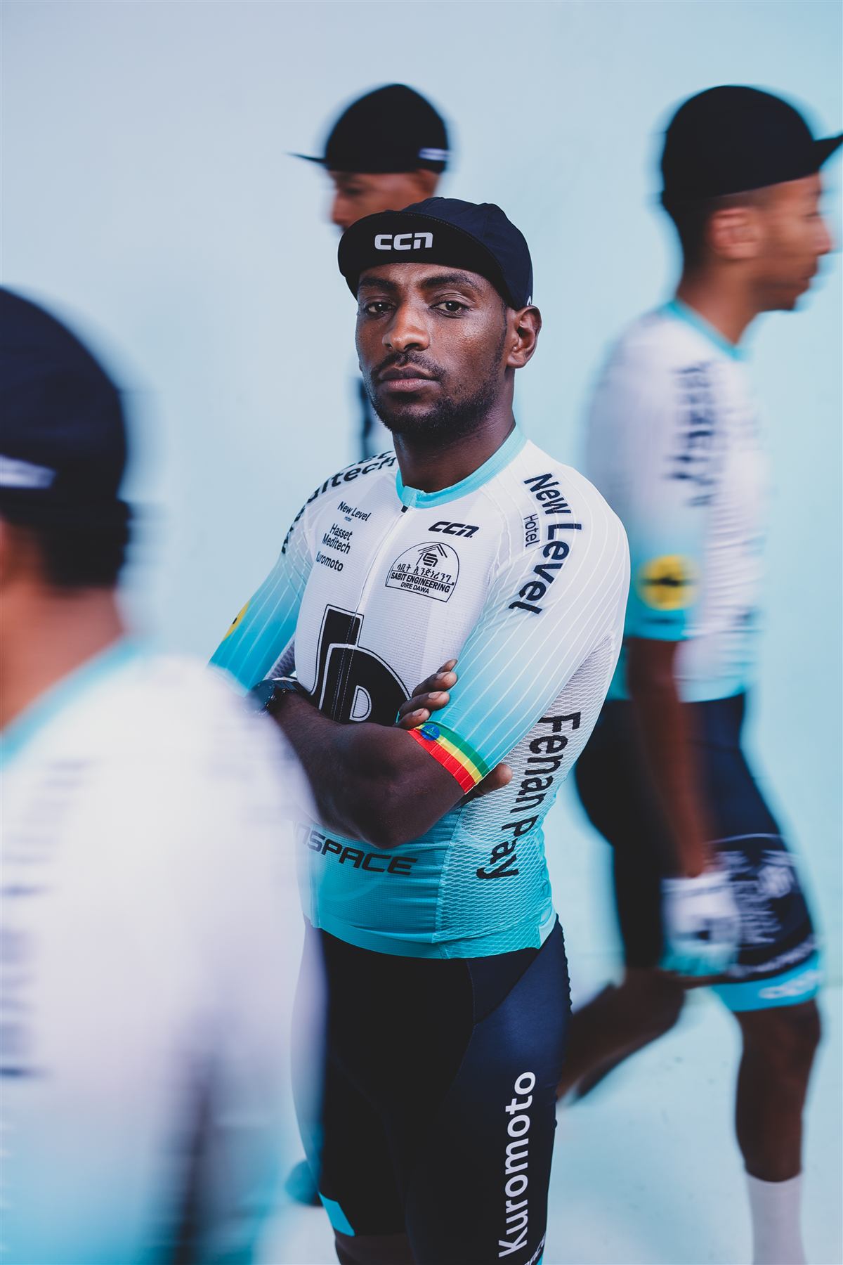 A rider with folded arms as teammates move past in motion blur