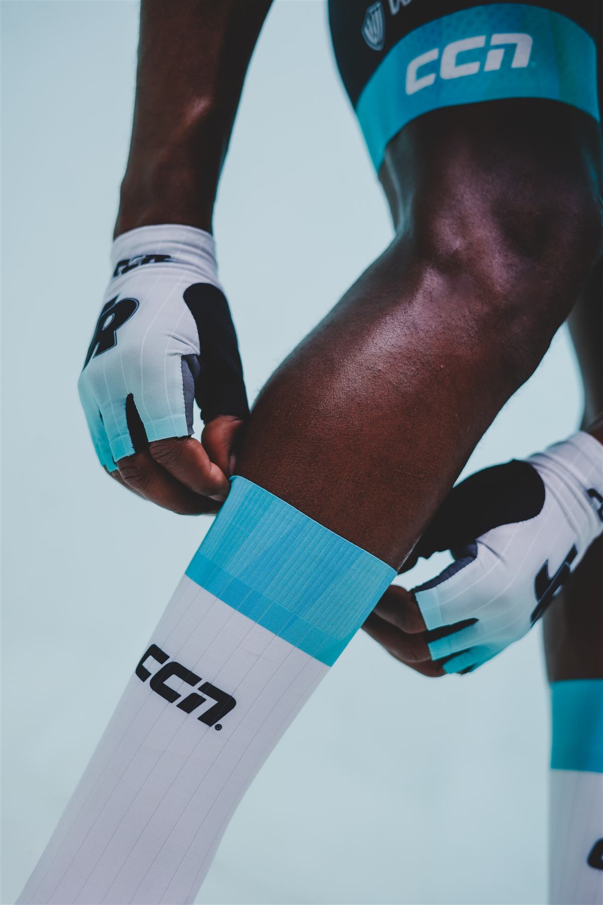 A rider adjusting a white sock with the aqua cuff