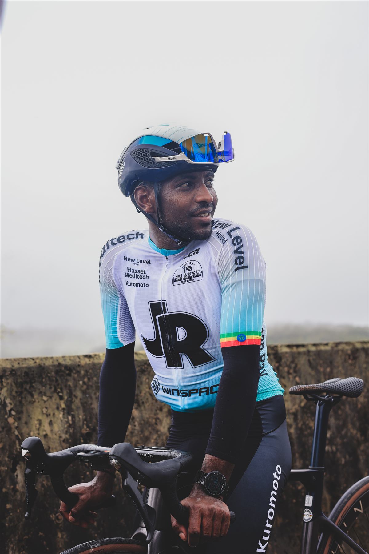 A rider smiling beside his bike on a misty road